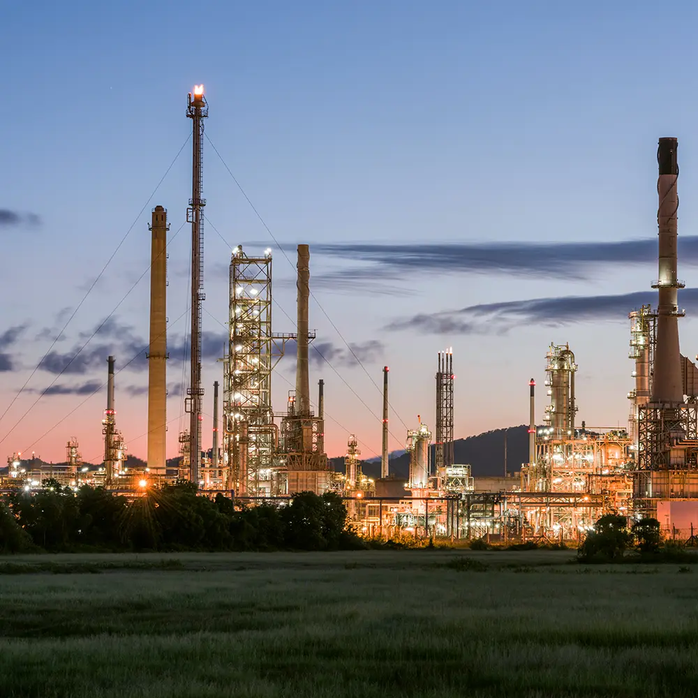 Industrial oil refinery and chemical plant illuminated at dusk with a field in the foreground